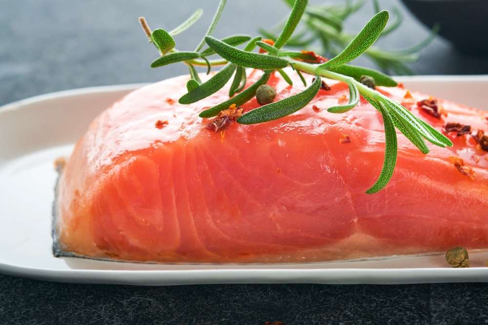 Salmon fish piece. Fresh raw salmon fish piece on marble board stand with herbs and lemon on black background. Seafood or menu concept. Top view.