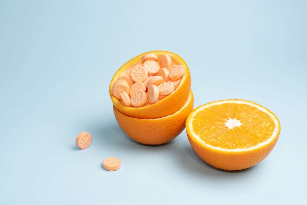 Half orange and peel with vitamin C tablets on a blue background, close up. Vitamin C pills as an alternative to citrus fruits. Immune booster concept.